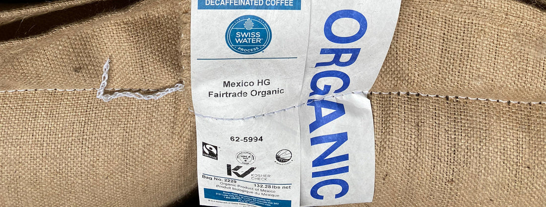 Blue white and black label sewn on to a jute coffee bag that says ORGANIC and displays several icons and symbols relating to certifications for Swiss Water Decaf Coffee.