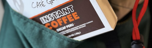 White, brown and orange box of Decaf Instant Coffee tucked into a green travel bag. Swiss Water Decaf Instant Coffee The Travel Hero