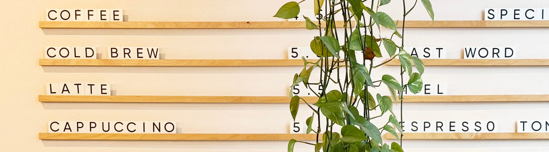 Cafe menu with various drinks in block letters on wooden rails. A green hanging plant dangles in front. Swiss Water Decaf on the Menu Welcoming Decaf Drinkers to Your Cafe